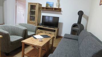 A living room with a television, two grey armchairs, a wooden coffee table, a cabinet, and a fireplace.