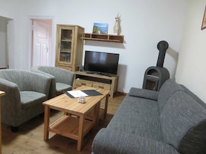 Una sala de estar con televisor, dos sillones grises, una mesa de centro de madera, un aparador y una chimenea.