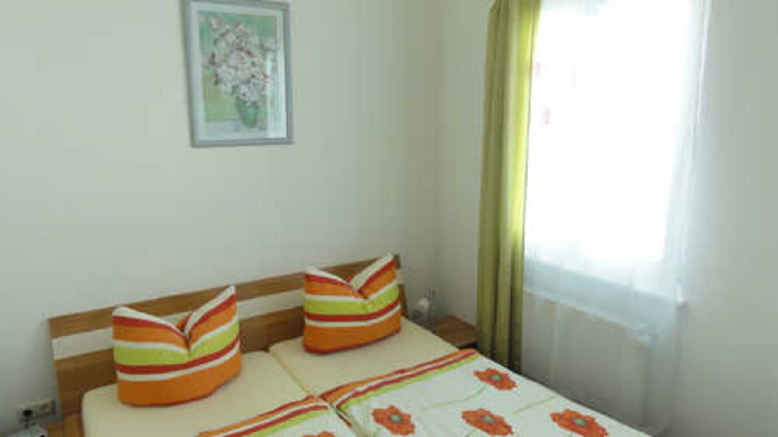 A room with a bed, pillows, a framed picture on the wall, and a window with curtains.