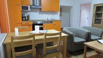 Una cocina compacta con armarios naranjas, microondas, estufa y una zona de comedor con mesa y sillas.