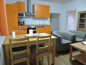 Een compacte keuken met oranje kastjes, een magnetron, fornuis en een eethoek met een tafel en stoelen.