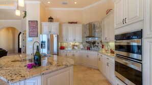 A kitchen with white cabinets, a granite countertop, stainless steel appliances, and a marble backsplash. - Luxury villa in a prime location with an oversized pool and whirlpool (Cape Coral)