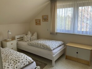 A bedroom with a single bed, a nightstand, a bedside table, a wardrobe, and a window with curtains.