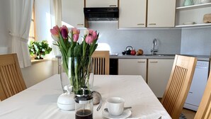 Une cuisine moderne avec des meubles blancs, une machine à café, un vase rempli de fleurs et une assiette avec un morceau de gâteau.