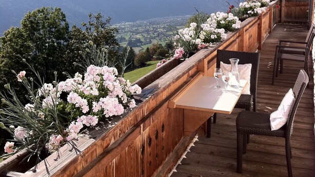 Une terrasse en bois avec une table et des chaises, offrant une vue sur un paysage montagneux.