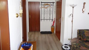 Un pasillo con una puerta de madera, un perchero, una mesita con un cuenco azul, una lámpara de pie y un sofá estampado.