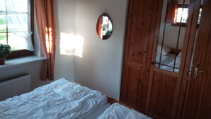 Un dormitorio con una cama, un armario de madera, una ventana con cortinas y una planta en maceta.