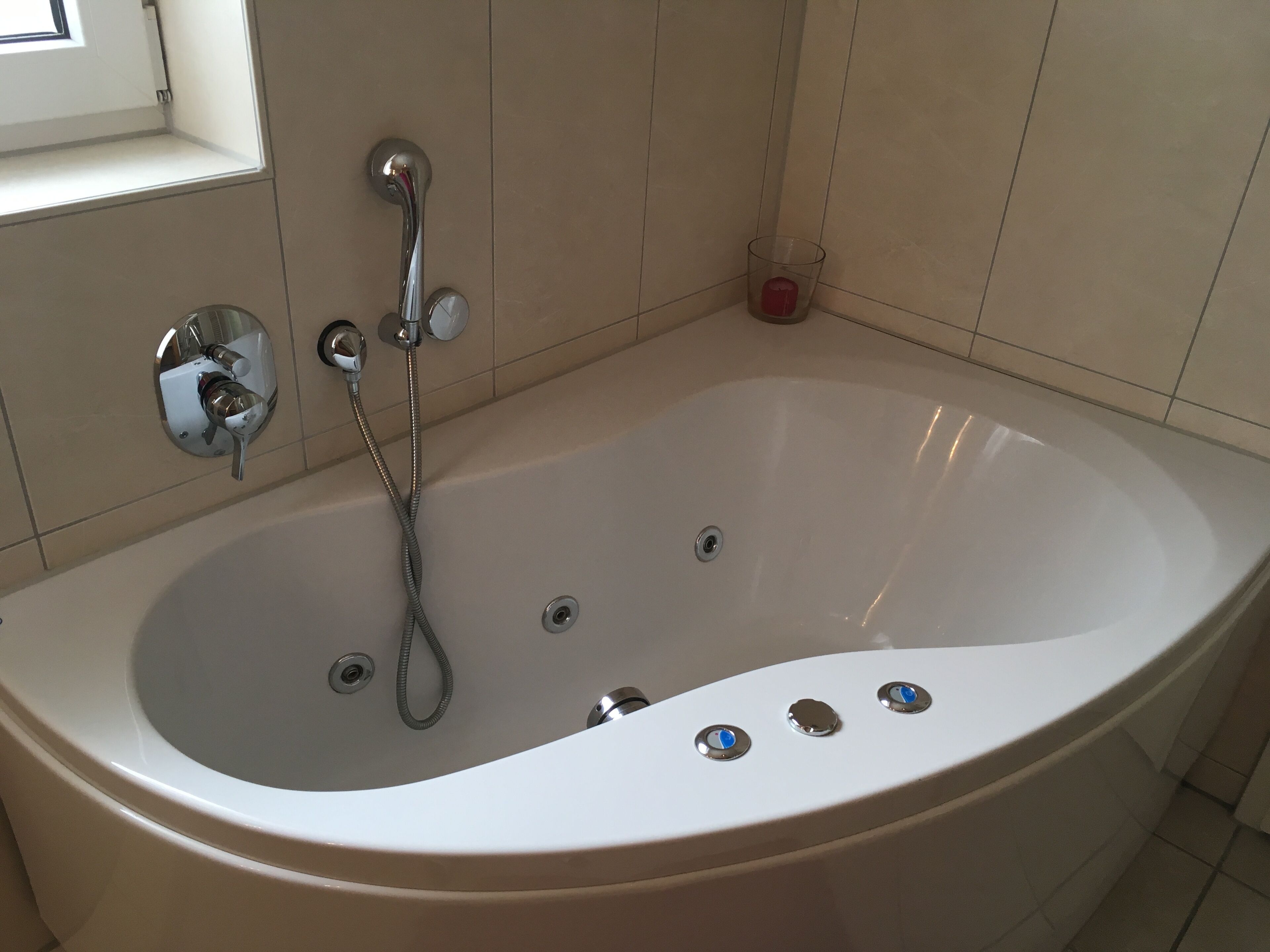 Un baño moderno con una bañera independiente, un cabezal de ducha de mano y un candelabro de vidrio.