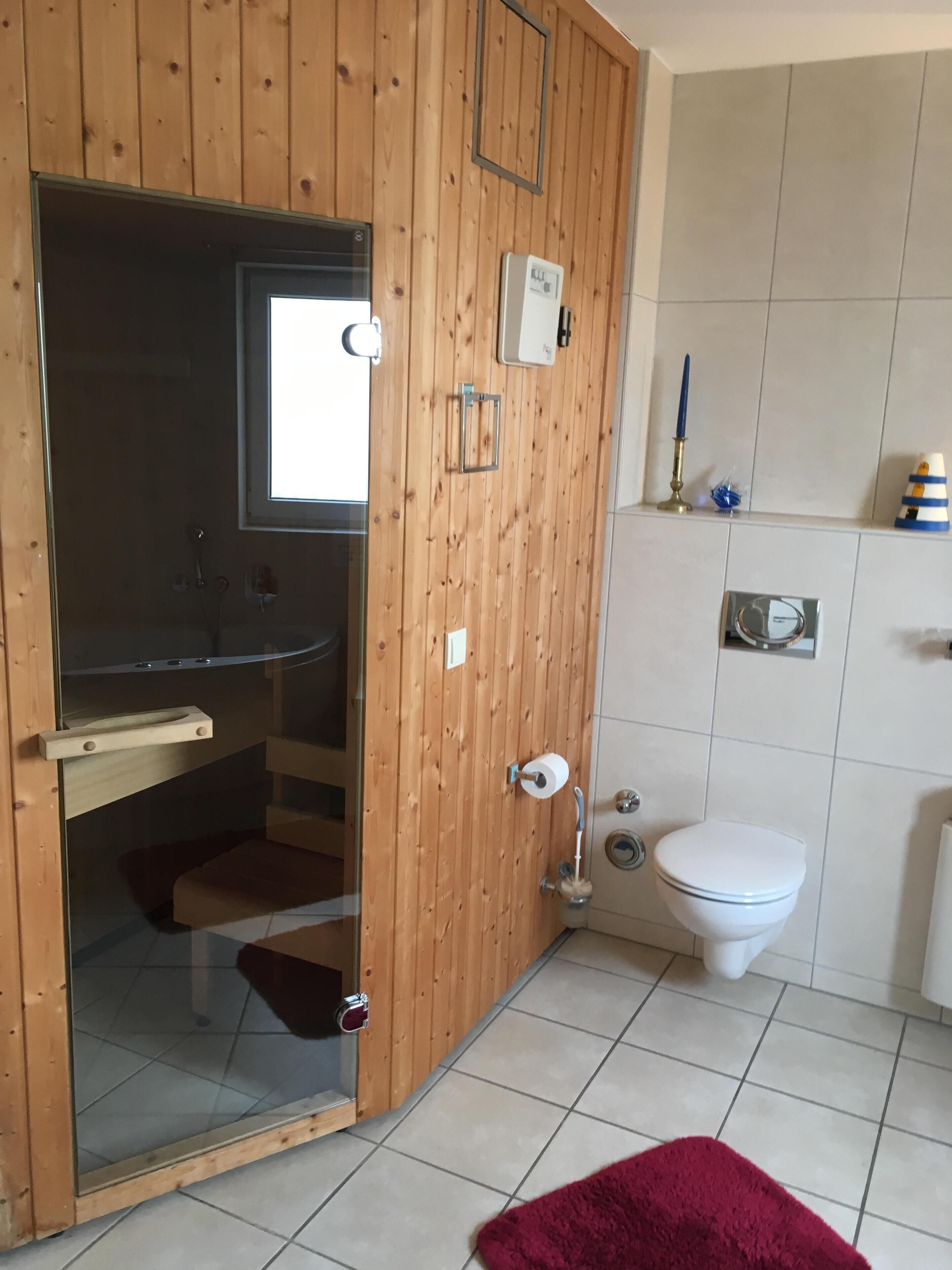 Ein Badezimmer mit Holztür, Toilette, Bidet und einer Duschkabine aus Glas.
