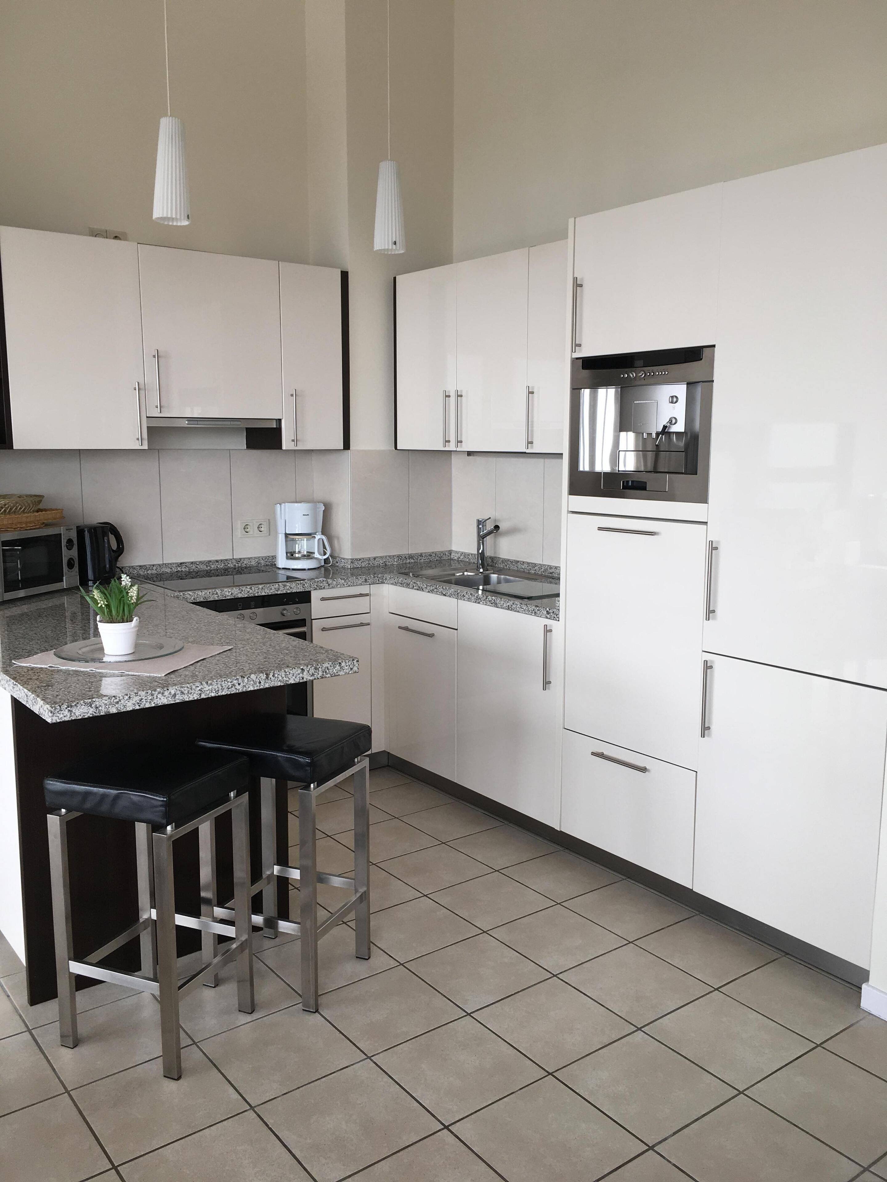 Una cocina moderna con armarios blancos, horno empotrado, cafetera y refrigerador de acero inoxidable.