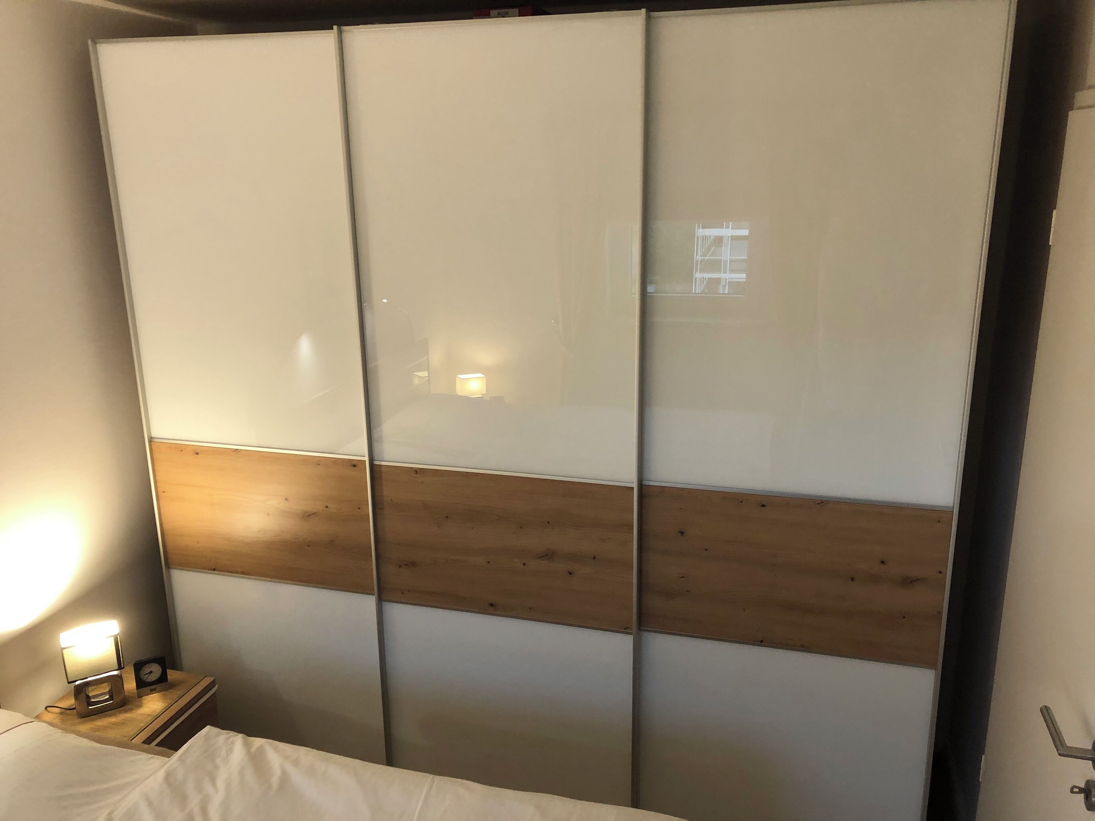Una habitación con cama, una mesita de noche con lámpara y un armario corredero con panel de madera.