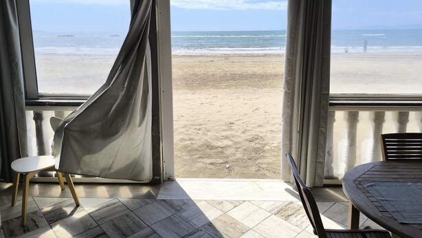 A room with a beach view through large windows, a chair, and a table. - Casa Viale Italia - homely house with direct access to the sandy beach (Follonica)