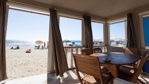 A sunlit patio with a wooden table and chairs, overlooking a beach with umbrellas and people. - Casa Viale Italia - homely house with direct access to the sandy beach (Follonica)