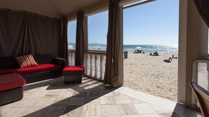 A room with a red sofa, a small table, and a view of a beach with people and an umbrella. - Casa Viale Italia - homely house with direct access to the sandy beach (Follonica)