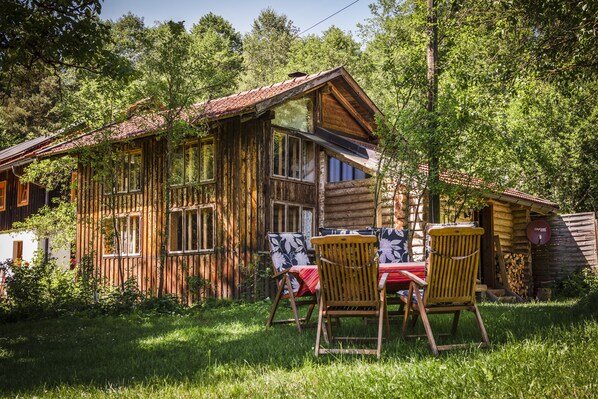 Eine rustikale Holzhütte mit geneigtem Dach, großen Fenstern und einem Essbereich mit zwei Stühlen und einem Tisch.