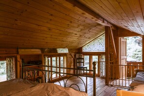 Una cabaña de madera con habitación en el altillo, un balcón con barandilla y vistas al bosque circundante.