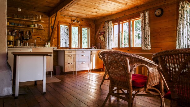 A wooden cabin interior with a kitchen area, wicker chairs, and a dining table. - Family-friendly holiday home in the most beautiful hiking area!  (Arnbruck)
