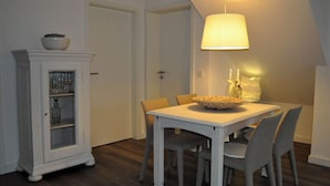 Un coin repas comprenant une table, des chaises, un buffet aux portes vitrées et une lampe suspendue.