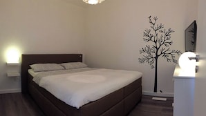 Une chambre à coucher avec un lit, des tables de chevet, un motif décoratif représentant un arbre appliqué sur le mur et une table de chevet avec une lampe.