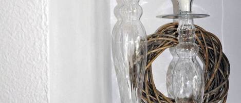 Two clear glass candle holders with white candles on a white shelf against a textured white wall.