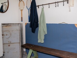Ein Zimmer mit einer Bank, einem Kleiderständer mit Tennisschlägern und einem Metallschrank.