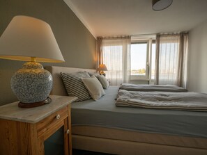 A bedroom with a bed, bedside table, lamp, and window with curtains.