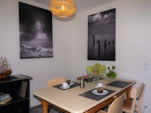 A dining area with a table, chairs, a ship model, and two framed photographs on the wall.