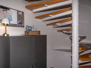 Eine Treppe mit Holzdielen und einer weißen Mittelstütze, ein grauer Aktenschrank mit Lampe sowie ein Schwarzes Brett mit verschiedenen Papieren und einer Karte.
