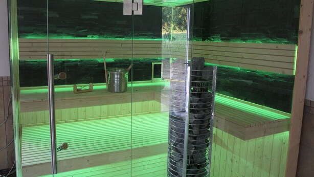 Un sauna doté d’une paroi en verre, de bancs en bois et d’un éclairage intérieur de couleur verte.