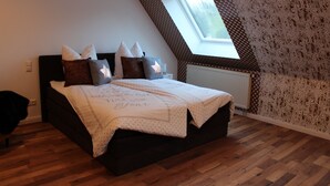 Une chambre avec un plafond en pente, un puits de lumière, un lit recouvert d’une courtepointe blanche et un papier peint à motifs.