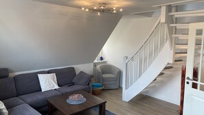 Uma sala de estar moderna com um sofá cinzento, uma mesa de centro de madeira e uma escadaria para um andar superior.