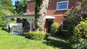 A brick house with a covered patio, a tree, and a garden with various plants and flowers. - FH / Central to the Baltic Sea/North Sea/Denmark/Sylt/Amrum/Föhr (Stadum)