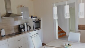 A modern kitchen with white cabinets, stainless steel appliances, and a wooden dining table with a bowl of fruit. - FH / Central to the Baltic Sea/North Sea/Denmark/Sylt/Amrum/Föhr (Stadum)