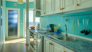 Una cocina con paredes color turquesa, gabinetes blancos y un lavamanos de acero inoxidable.