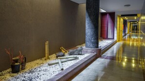 Un pasillo con piso de mármol, una columna y una pequeña zona de jardín con rocas y plantas.