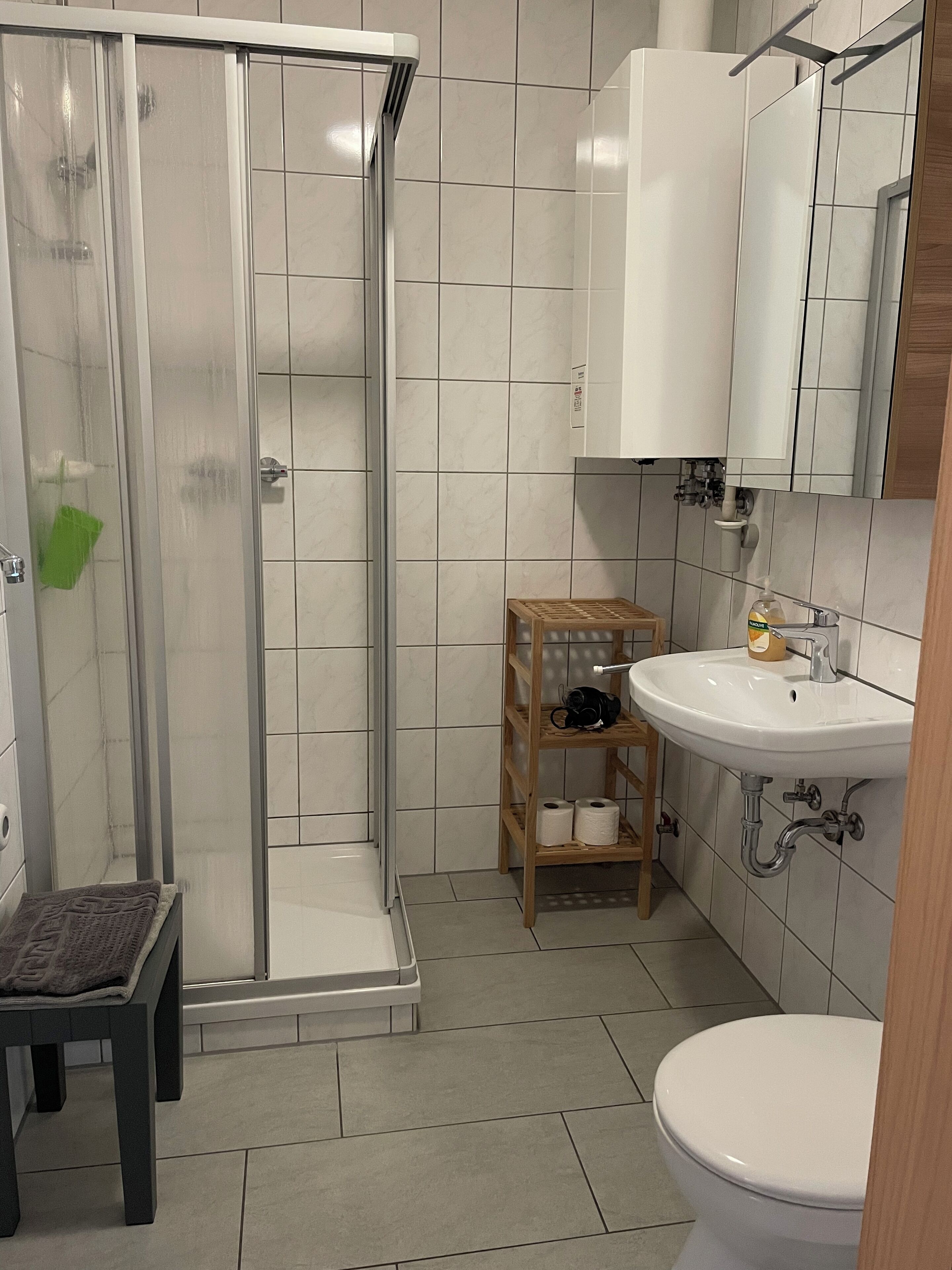 Ein Badezimmer mit Dusche, Toilette, Waschbecken und einem Holzregal.