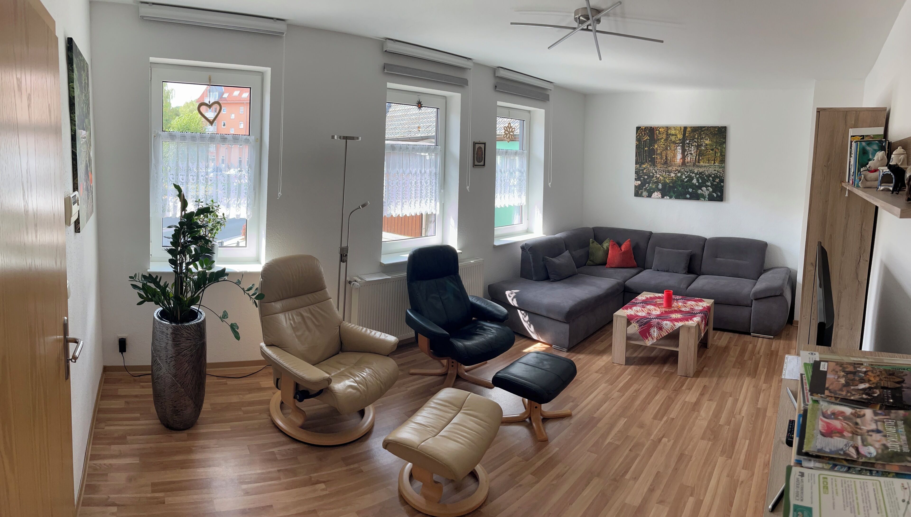 Ein Wohnzimmer mit grauem Sofa, zwei Sesseln, einem Couchtisch und einem Bücherregal.
