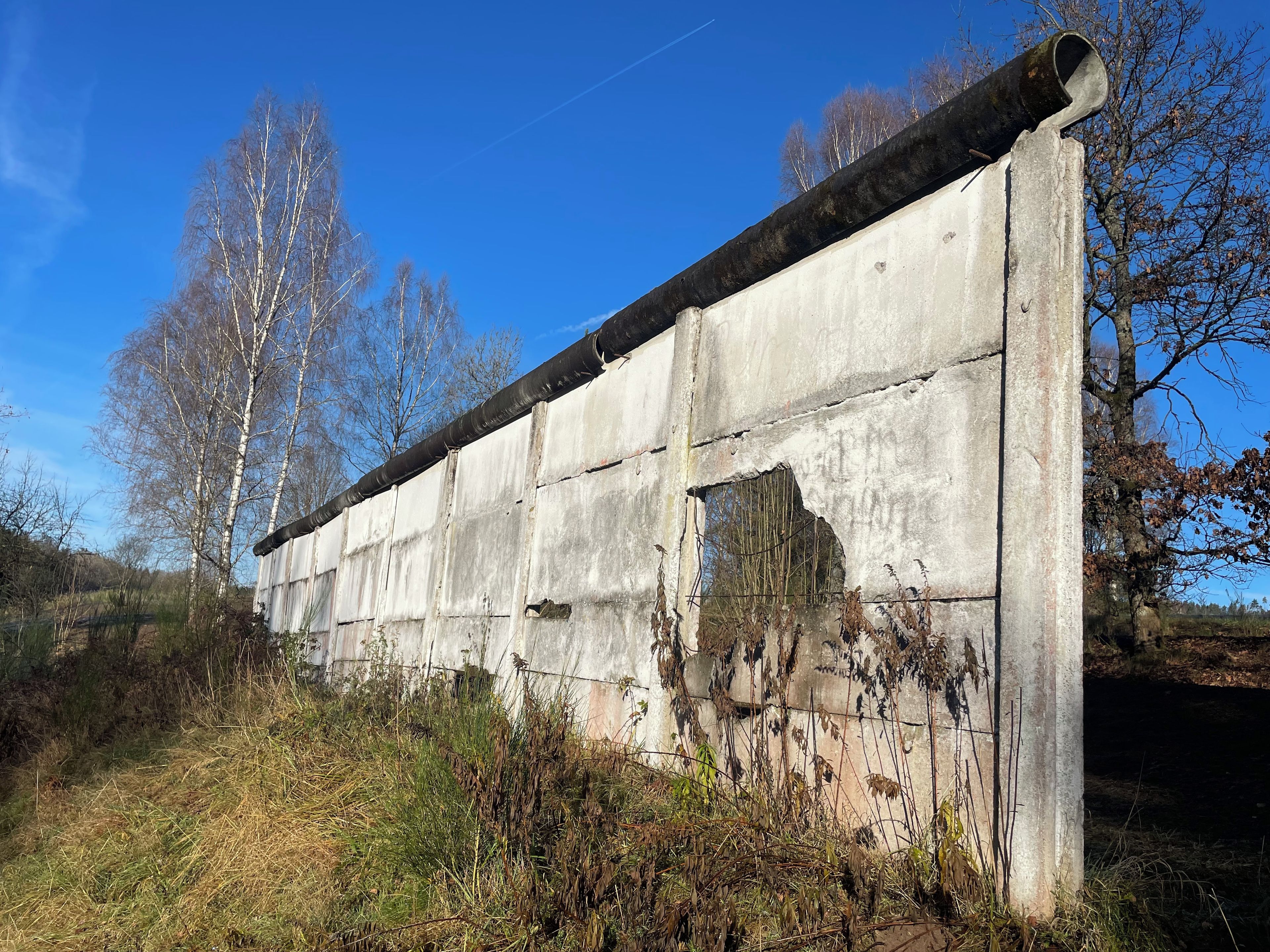 Une structure en béton dont une partie est endommagée, entourée de végétation et d’arbres.