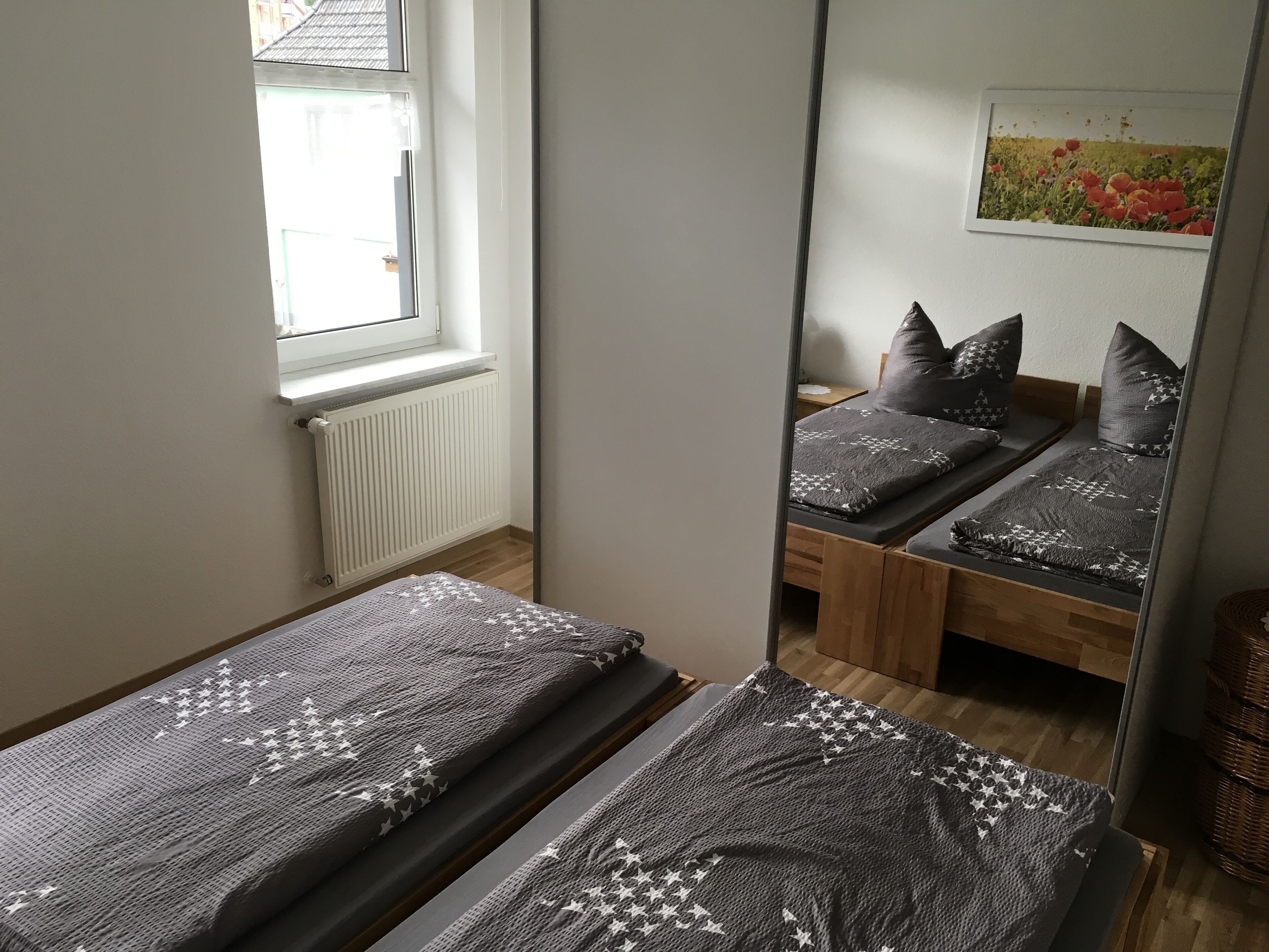 Et soveværelse med to enkeltsenge, en radiator, et vindue og et spejl der reflekterer rummet.