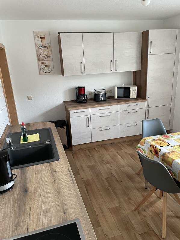 Een kleine keuken met een spoelbak, een magnetron, een koffiezetapparaat en een eethoek met een tafel en stoelen.