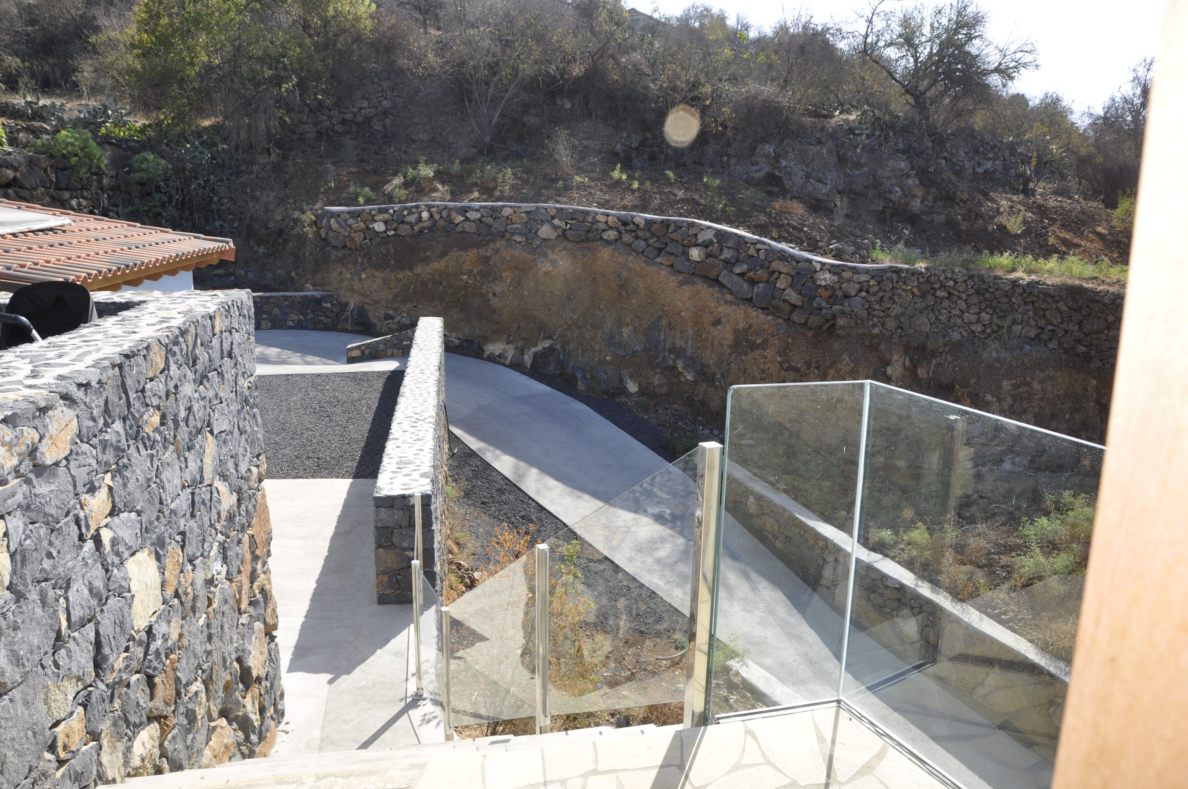 A stone retaining wall with a curved pathway leading to a glass railing overlooking a rocky hillside.
