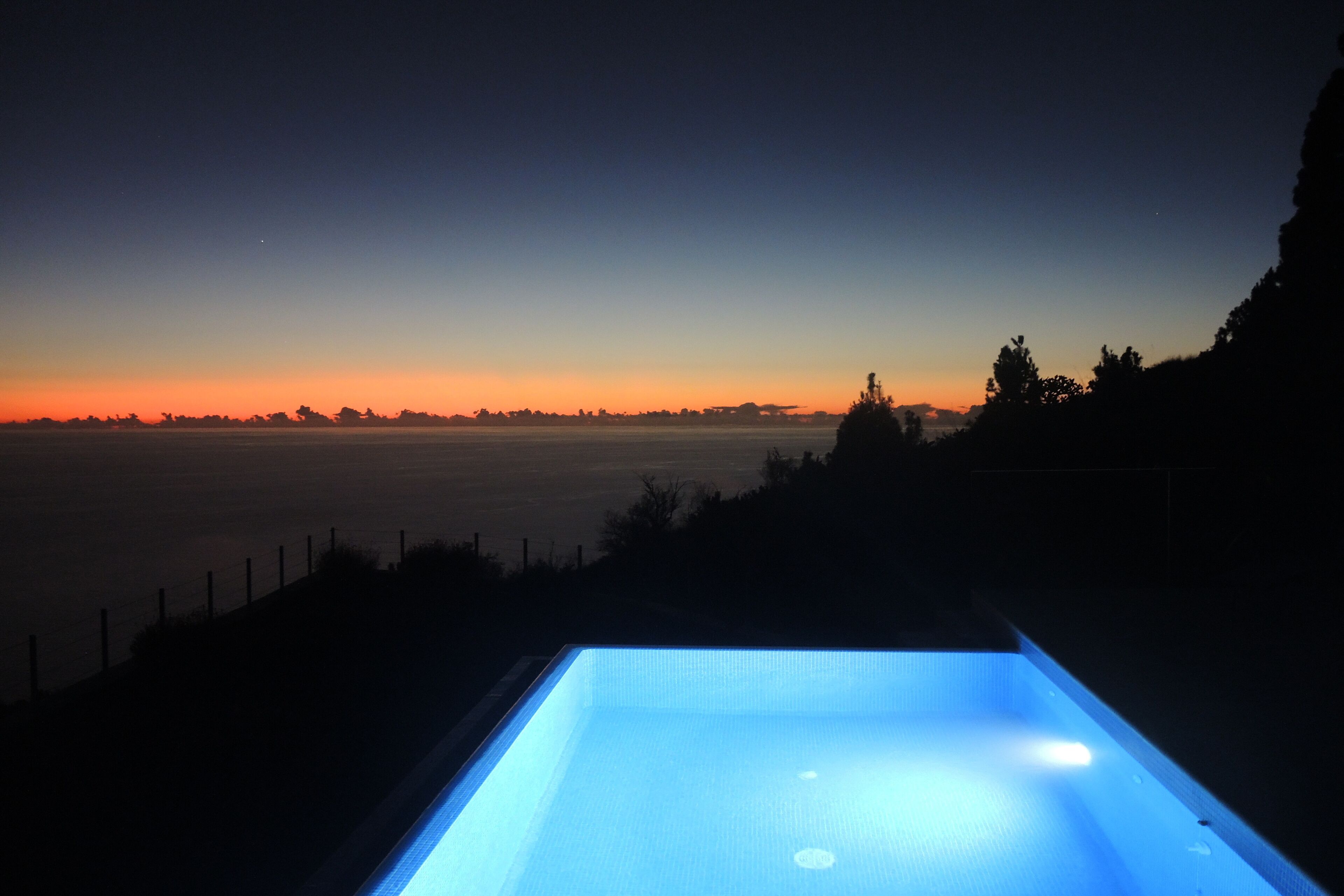 Ein Schwimmbad im Abendlicht mit Blick auf den Horizont und entfernte Bäume.
