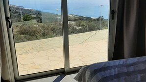 Ein Schlafzimmer mit einer großen Schiebetür, die auf eine Terrasse mit Blick auf das Meer und die Hügel führt.