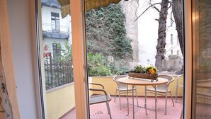Une terrasse avec une table ronde et des chaises, un pot de fleurs et une vue sur un immeuble et des arbres.