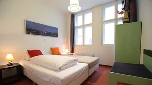 Une chambre d’hôtel avec deux lits, un bureau, une chaise, une table de chevet avec une lampe, une fenêtre avec des rideaux et un tableau au mur.