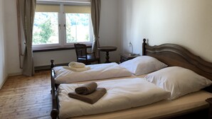 Hotelkamer met twee bedden, een stoel, een tafeltje en een raam met gordijnen.
