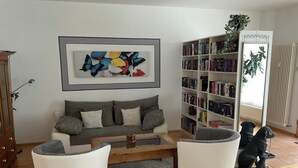 Un salon avec un canapé, deux fauteuils blancs, une table basse, une bibliothèque et un chien.