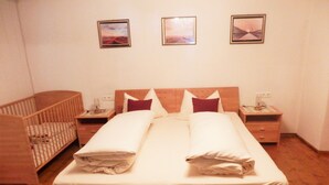 A neatly made bed with pillows, a wooden crib, and bedside tables with lamps. - Quaint farmhouse with comfort and a typical atmosphere (Biberwier)