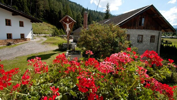 A rural setting with a white building, a wooden structure, and a crucifix. - Quaint farmhouse with comfort and a typical atmosphere (Biberwier)