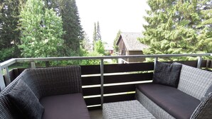 Ein aus Rattan gefertigtes Ecksofa mit passendem Fußhocker auf einem Balkon mit Metallgeländer.